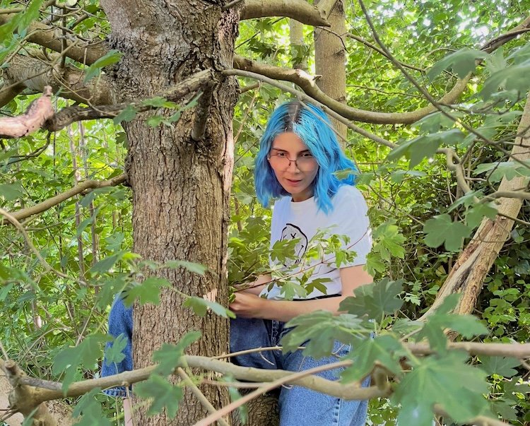 Vladyslava Bondar in a maple
              tree, holding a branch to protect against rusalky.